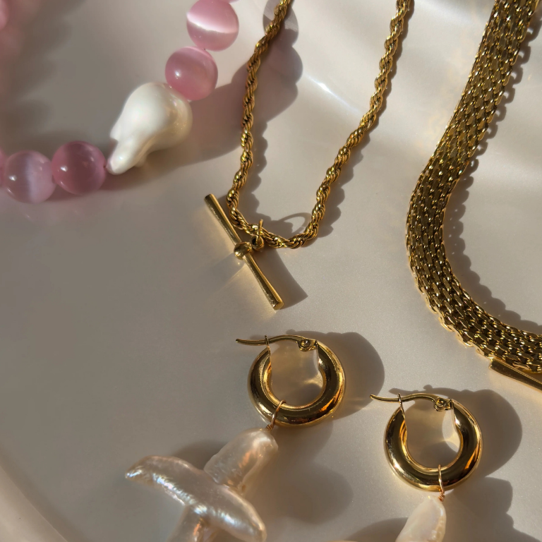 Gold jewelry including necklaces and earrings on a white surface with pink beads.