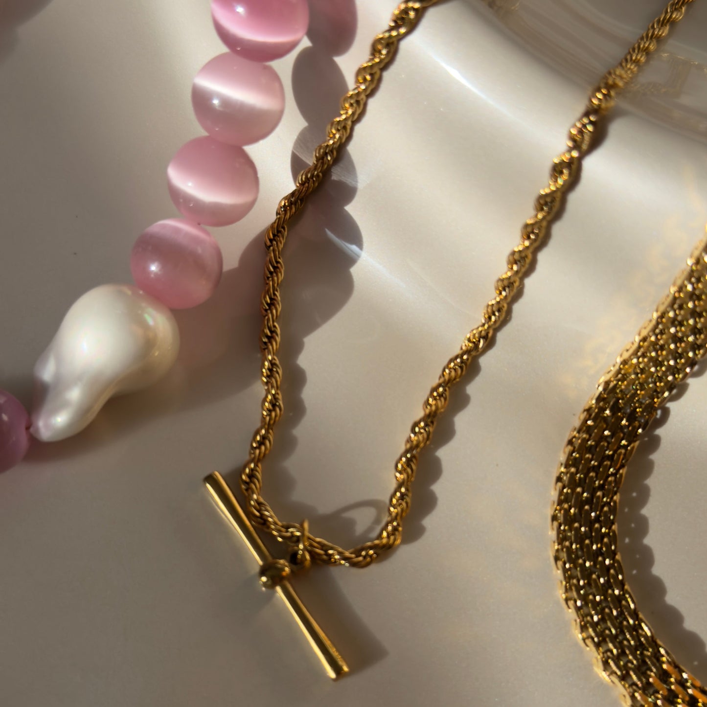 Gold necklace with a cross pendant and pink beaded bracelet on a white surface