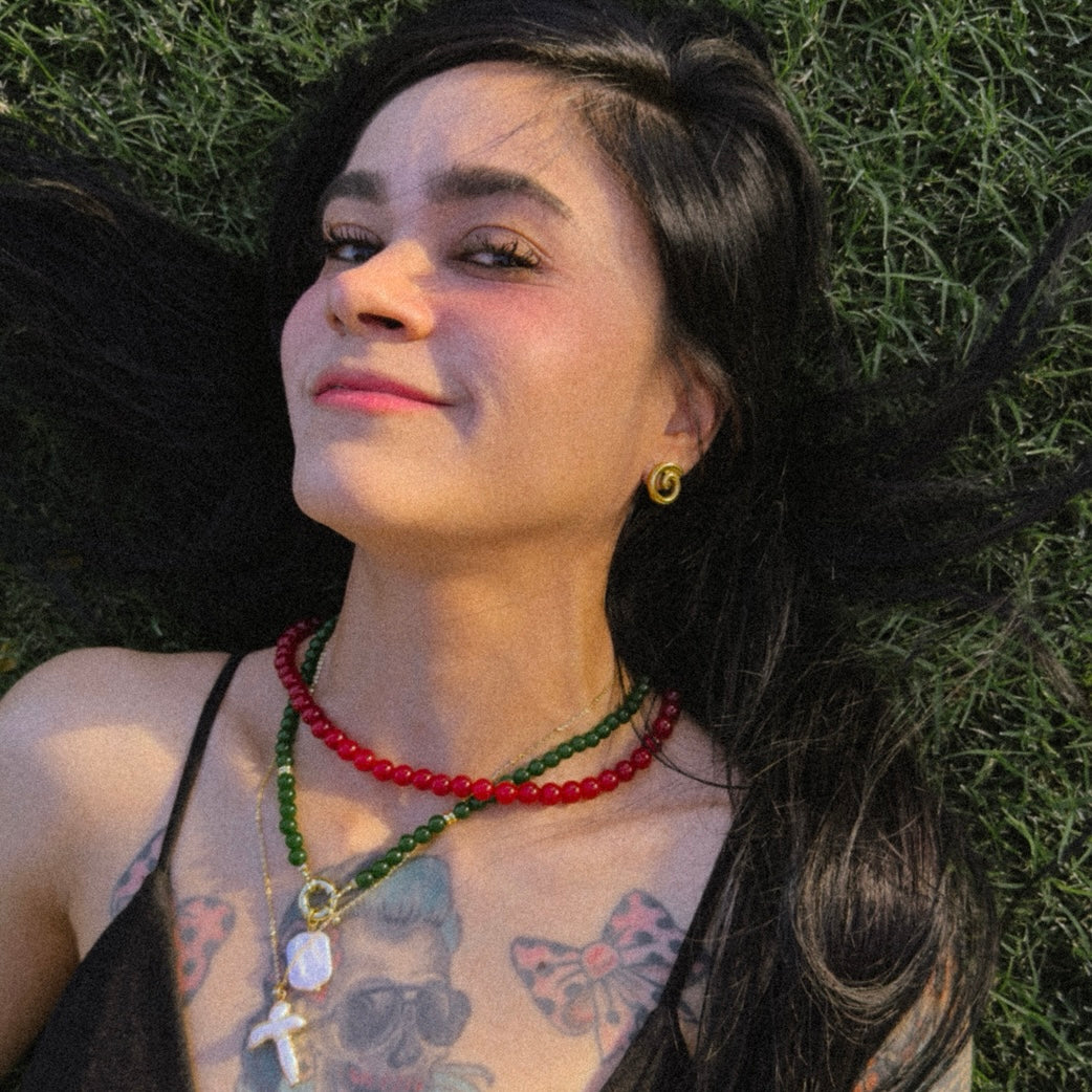 Person with tattoos and beaded necklaces lying on green foliage
