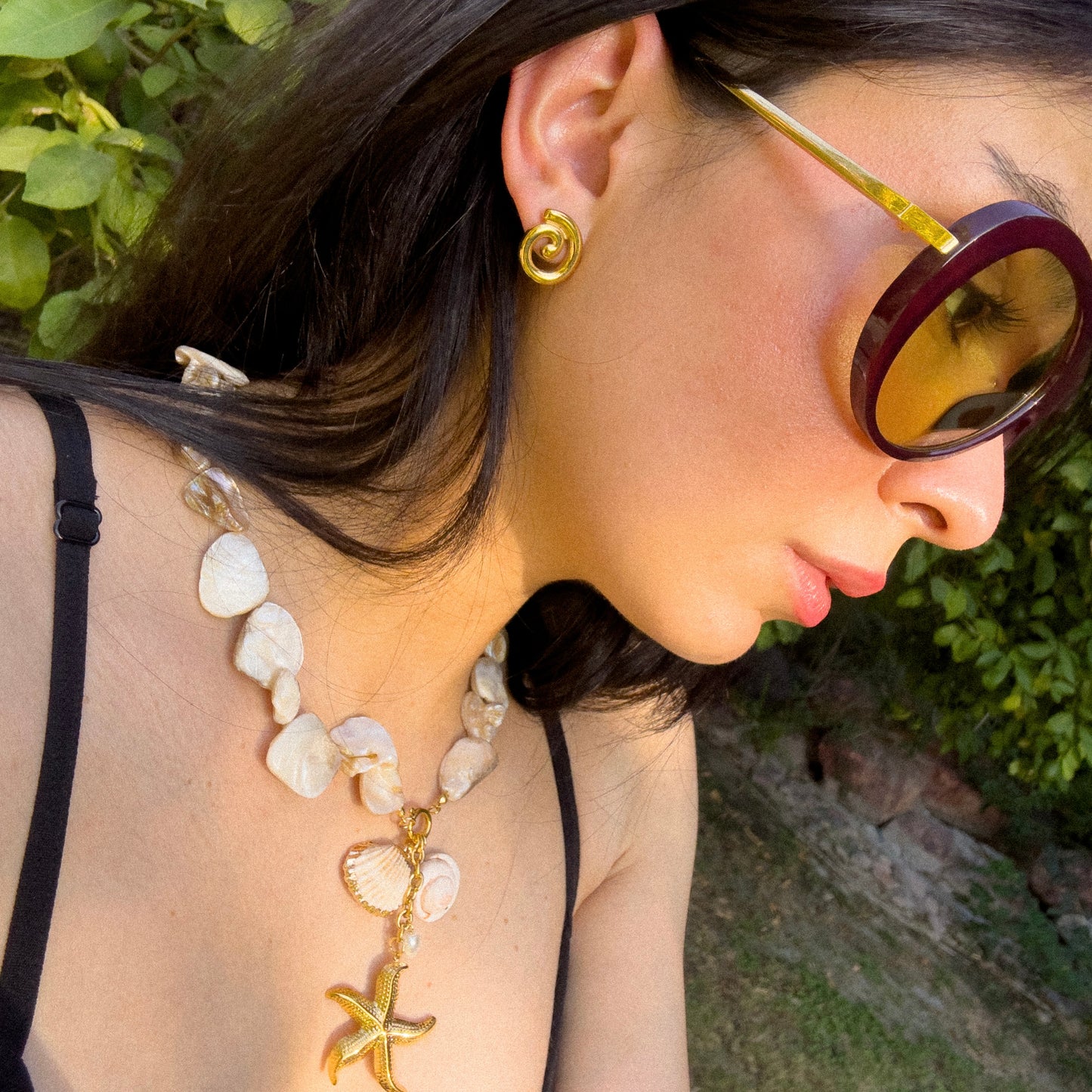 Woman wearing a necklace and sunglasses with a green outdoor background