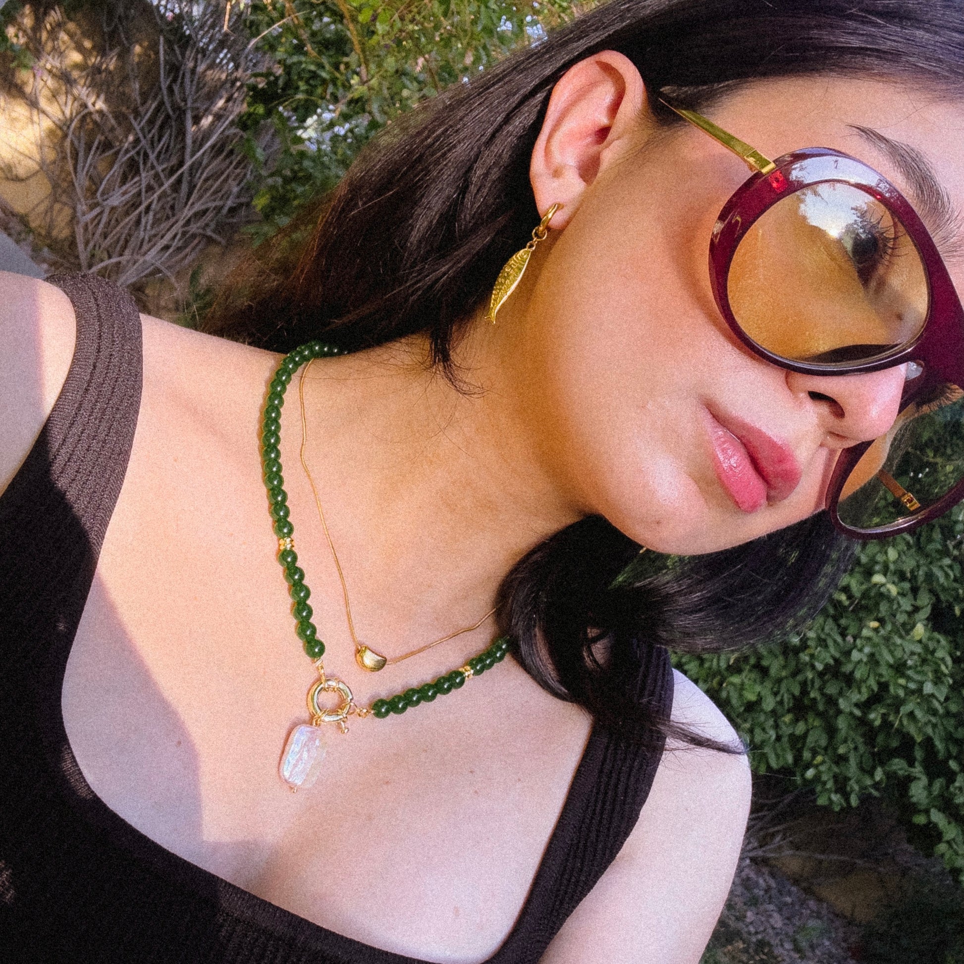 Woman wearing a green beaded necklace and gold earrings outdoors