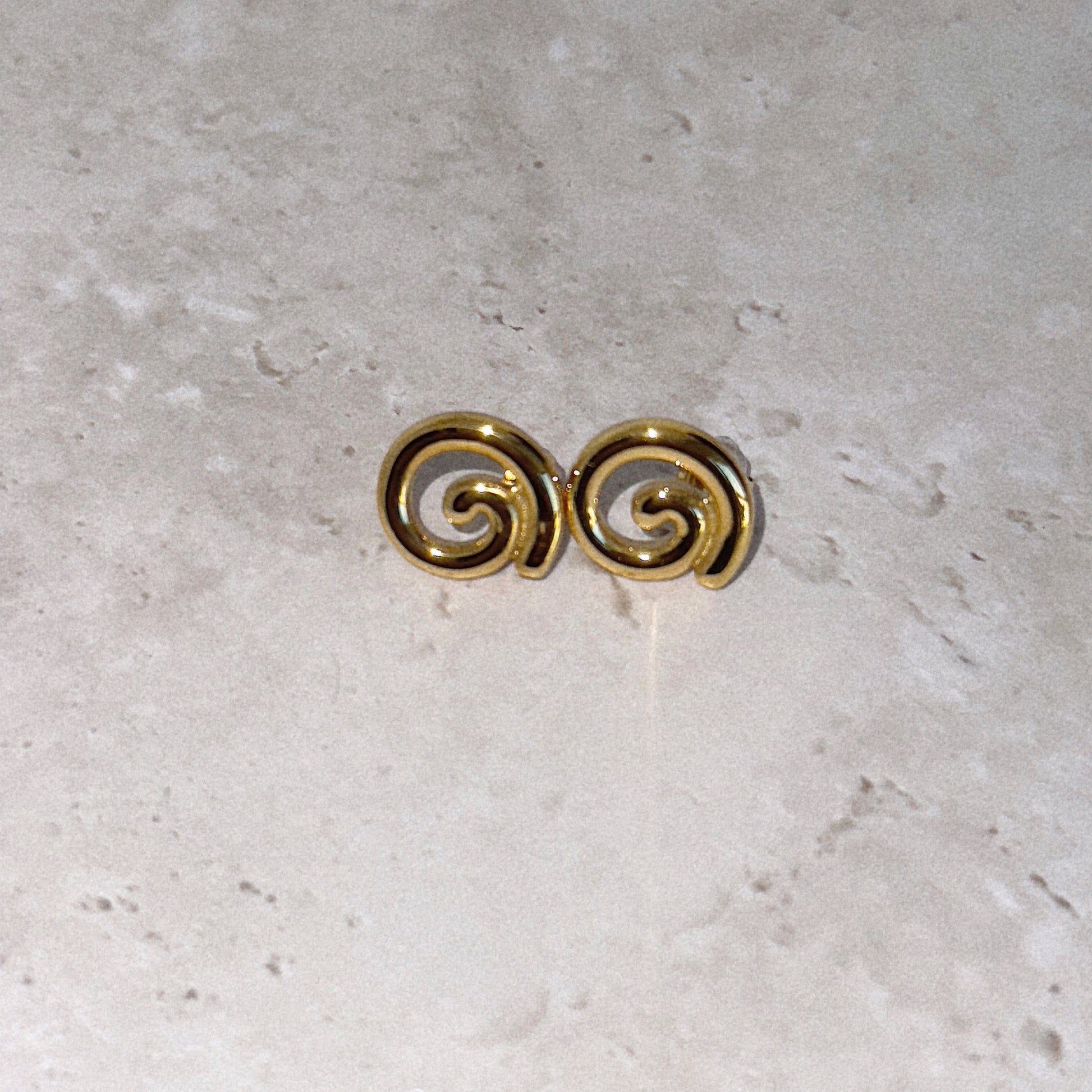 Gold spiral earrings on a light gray surface