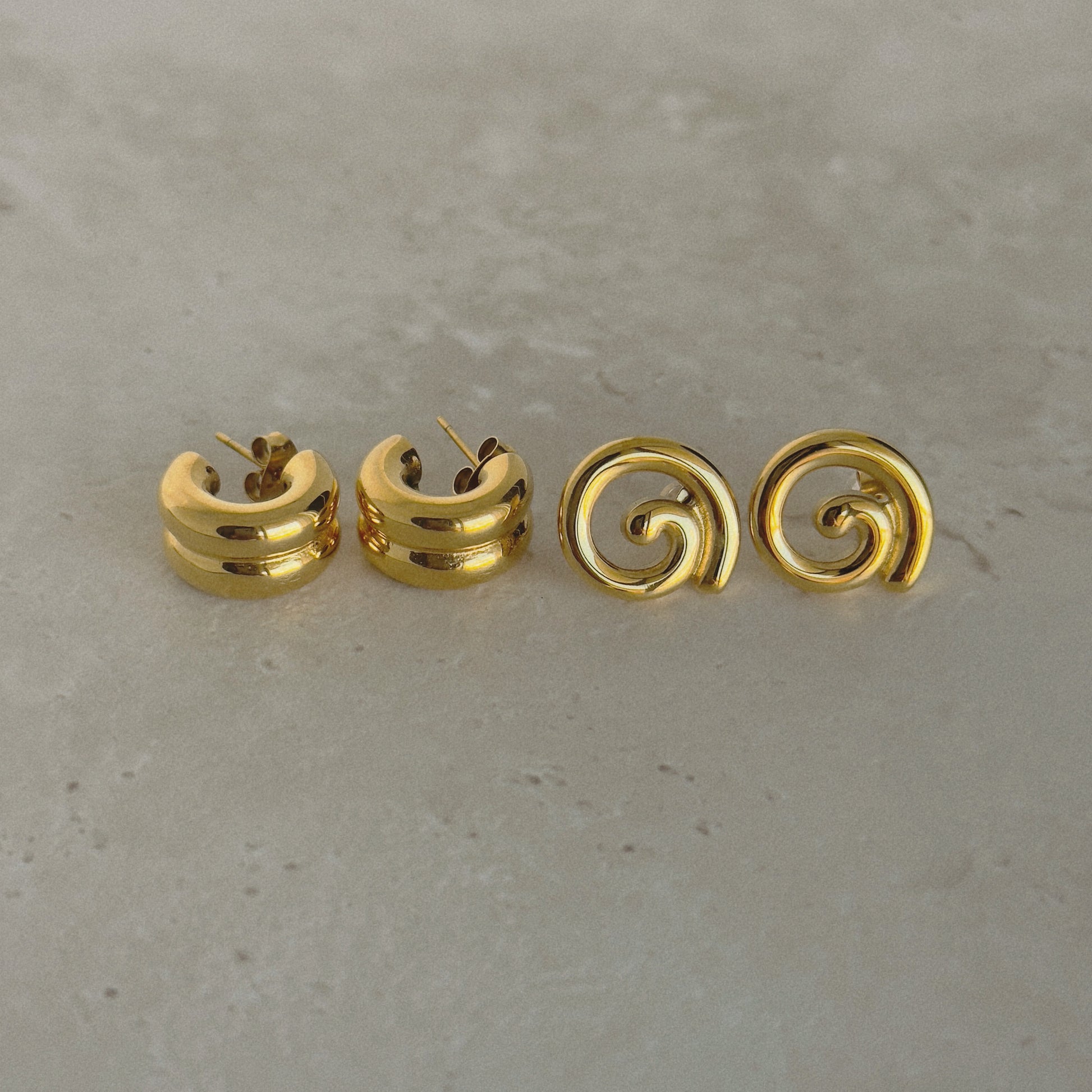 Four gold spiral earrings on a gray surface