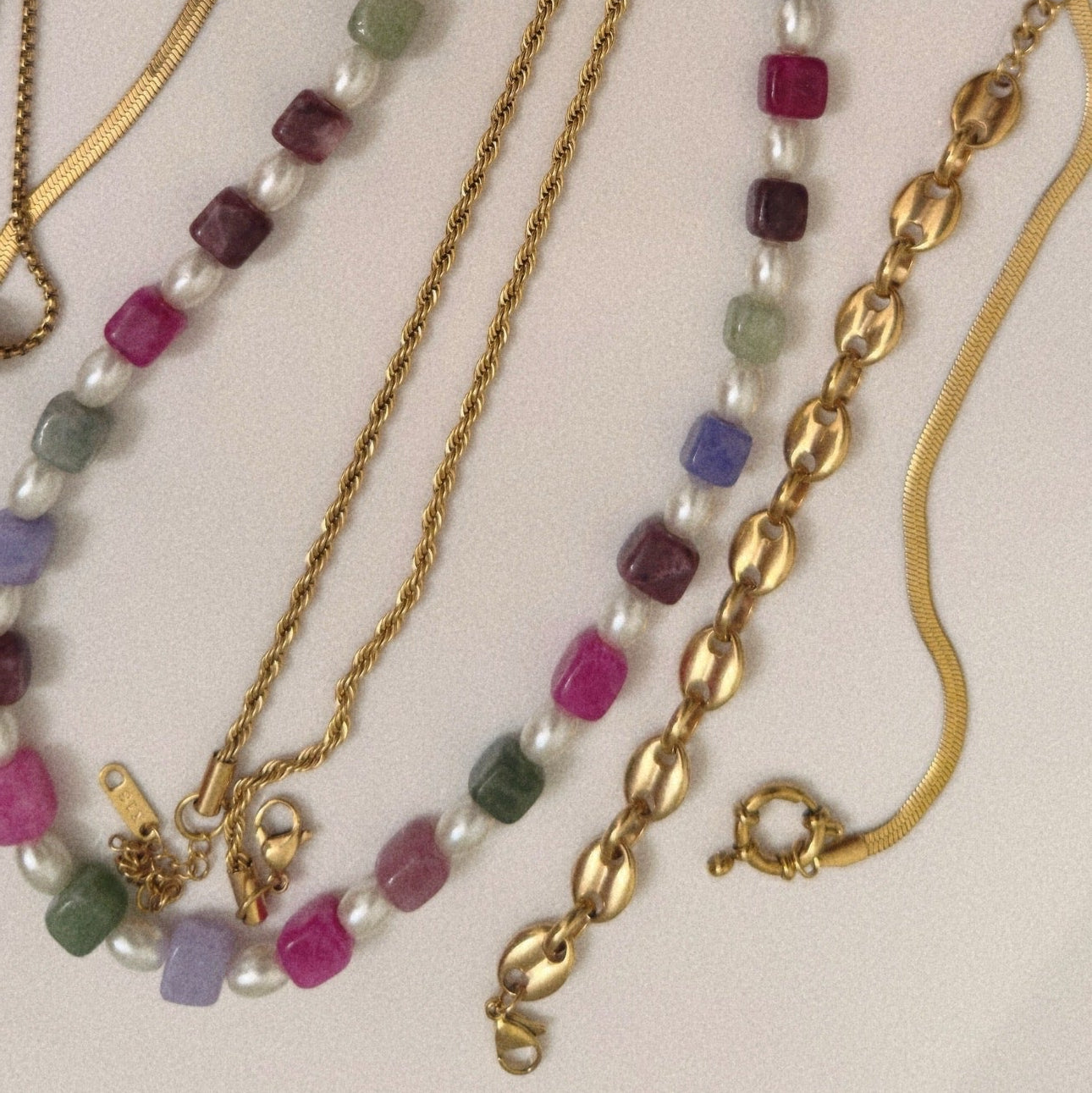 Gold chain necklaces with colorful beads on a light background